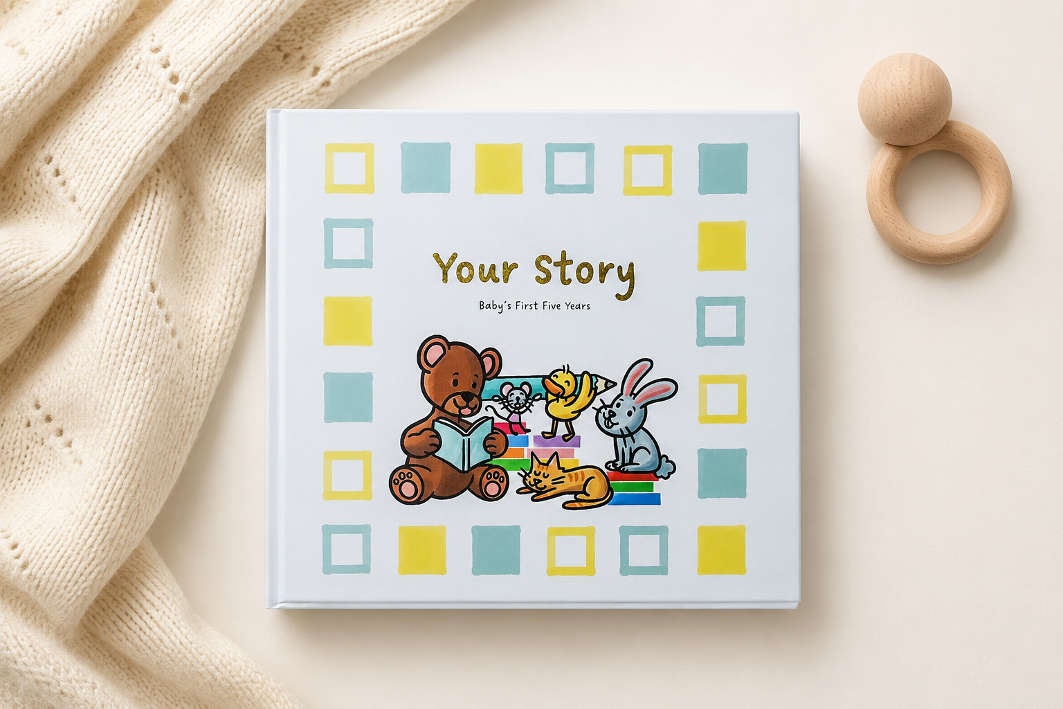 CLAENA baby memory book styled with a cream knit and wooden baby rattle